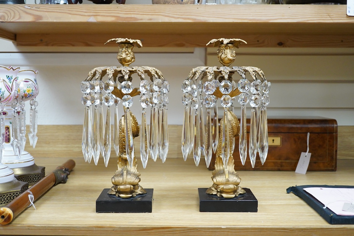 A pair of William IV gilt metal candlesticks, the stems formed as dolphins, with glass lustre drops, raised on square slate bases, 37cm high